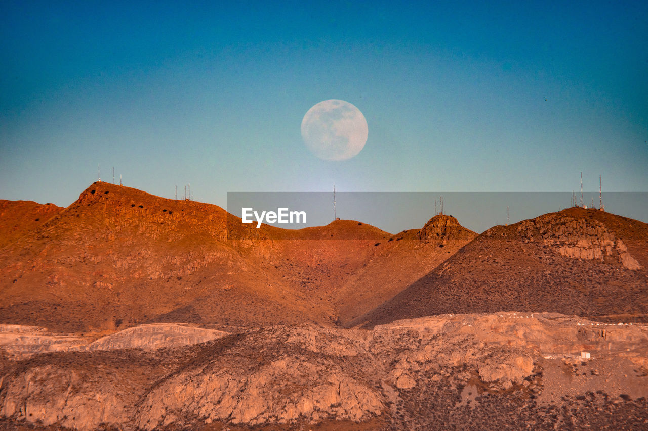 Scenic view of arid landscape against blue sky with full moon