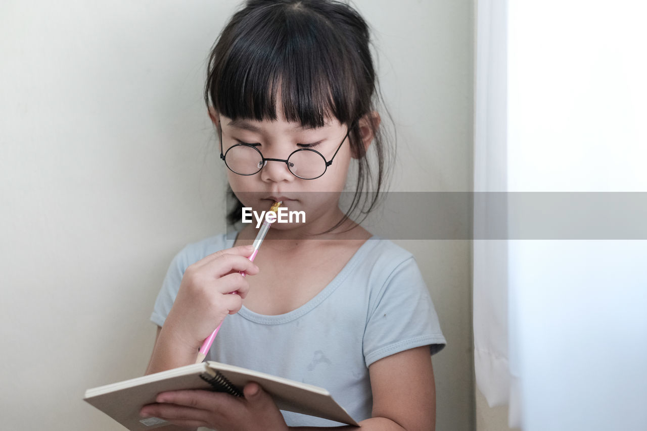 A child with glasses holding a pencil and write in the notebook intently. 