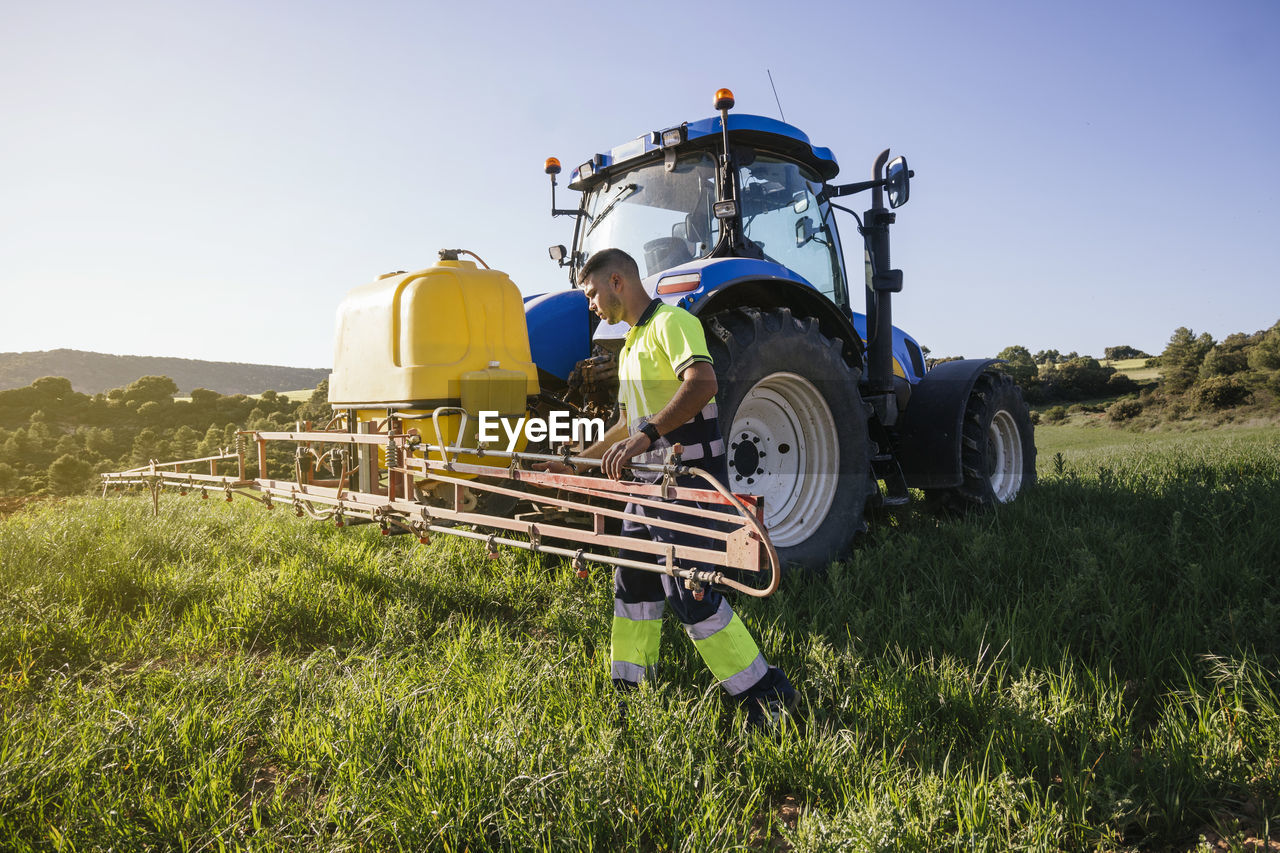 Young farmer adjusting crop sprayer on field on sunny day