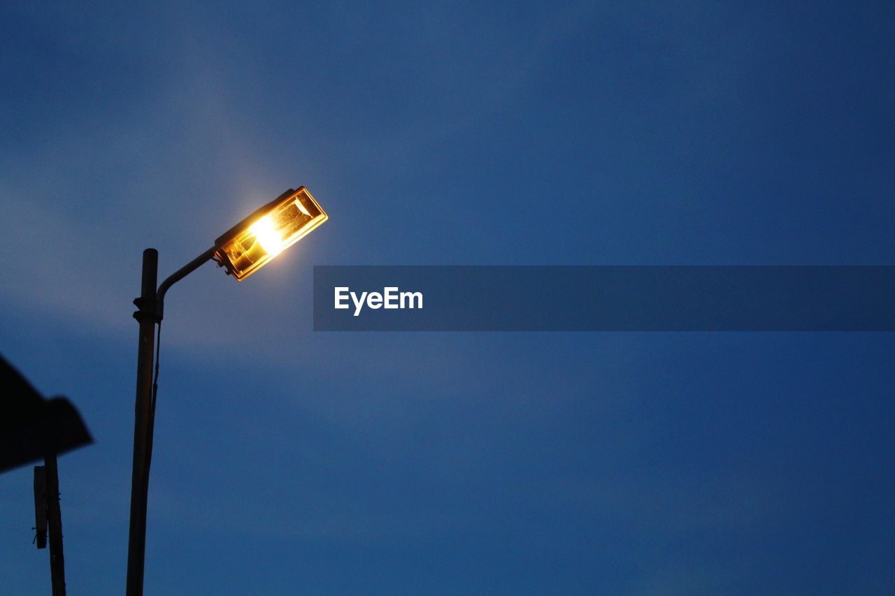 Low angle view of illuminated street light against blue sky