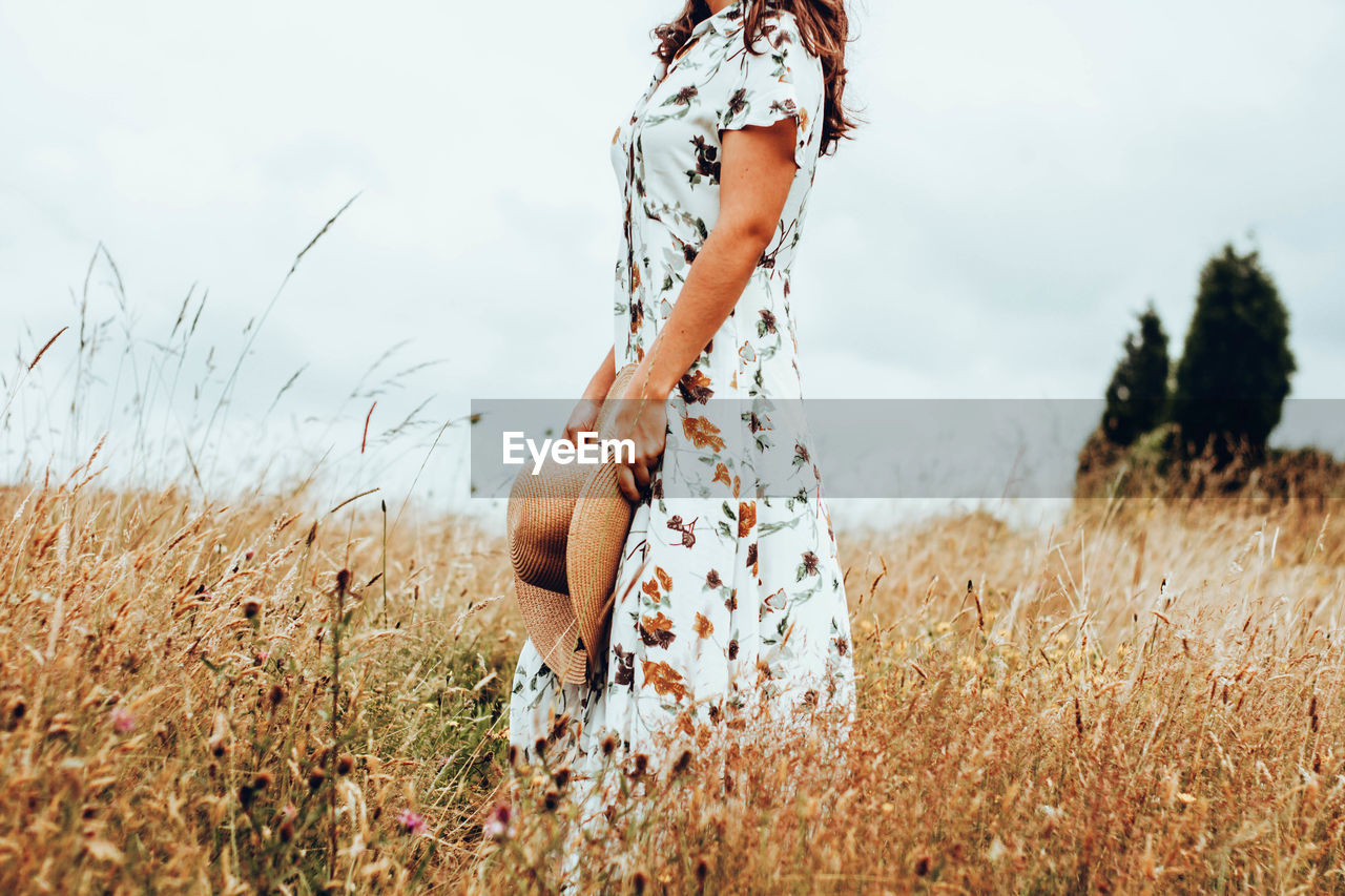 Midsection of woman standing on field against sky