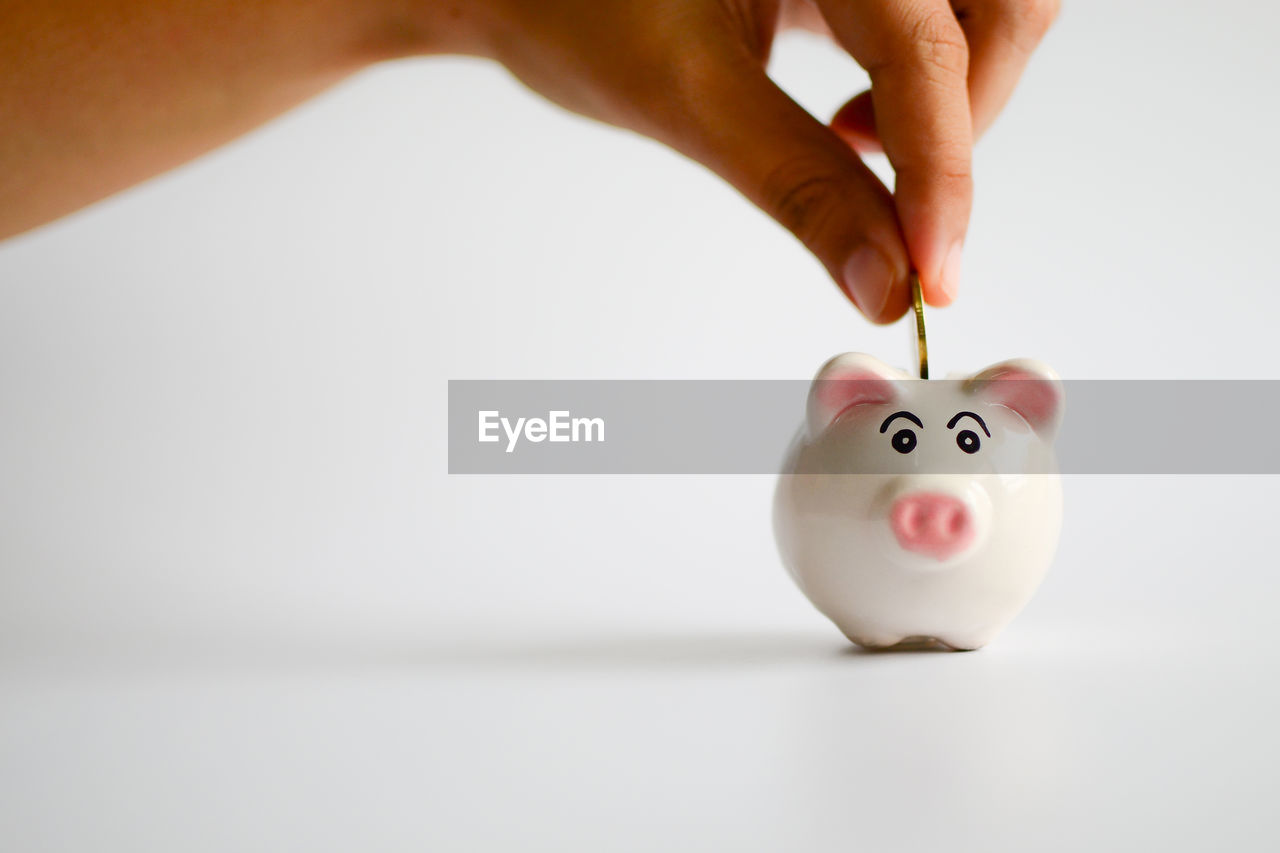Close-up of human hand and piggy bank against white background