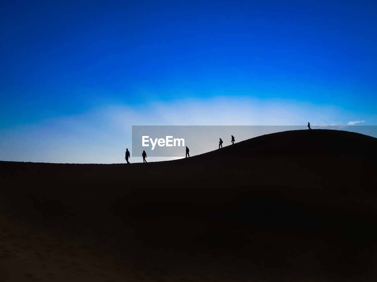 Silhouette people standing on desert against blue sky