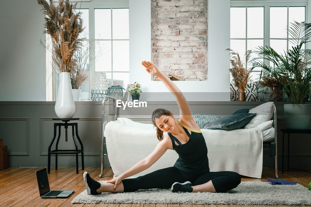 Positive athletic woman with neatly tied hair and tight sportswear stretching at home. 