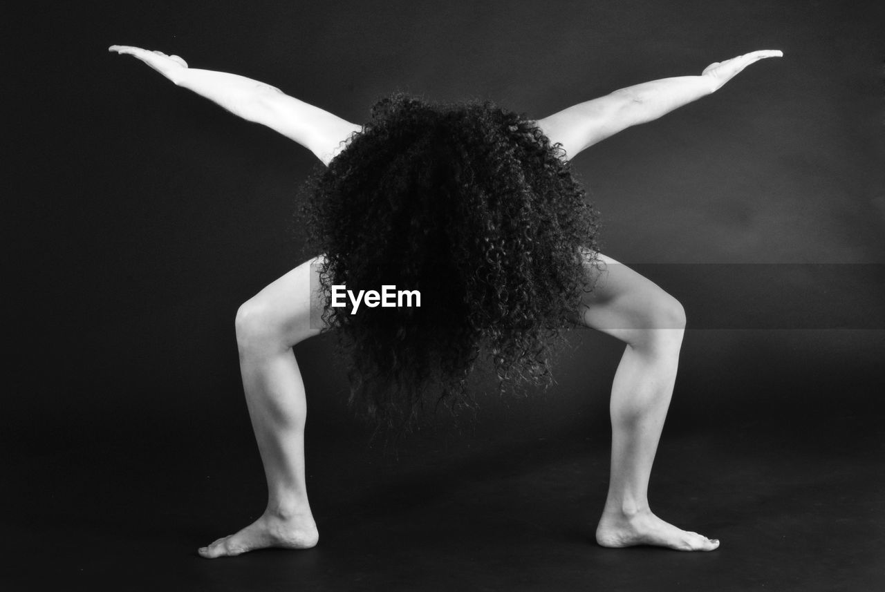 Naked woman with arms outstretched and curly hair standing against gray background