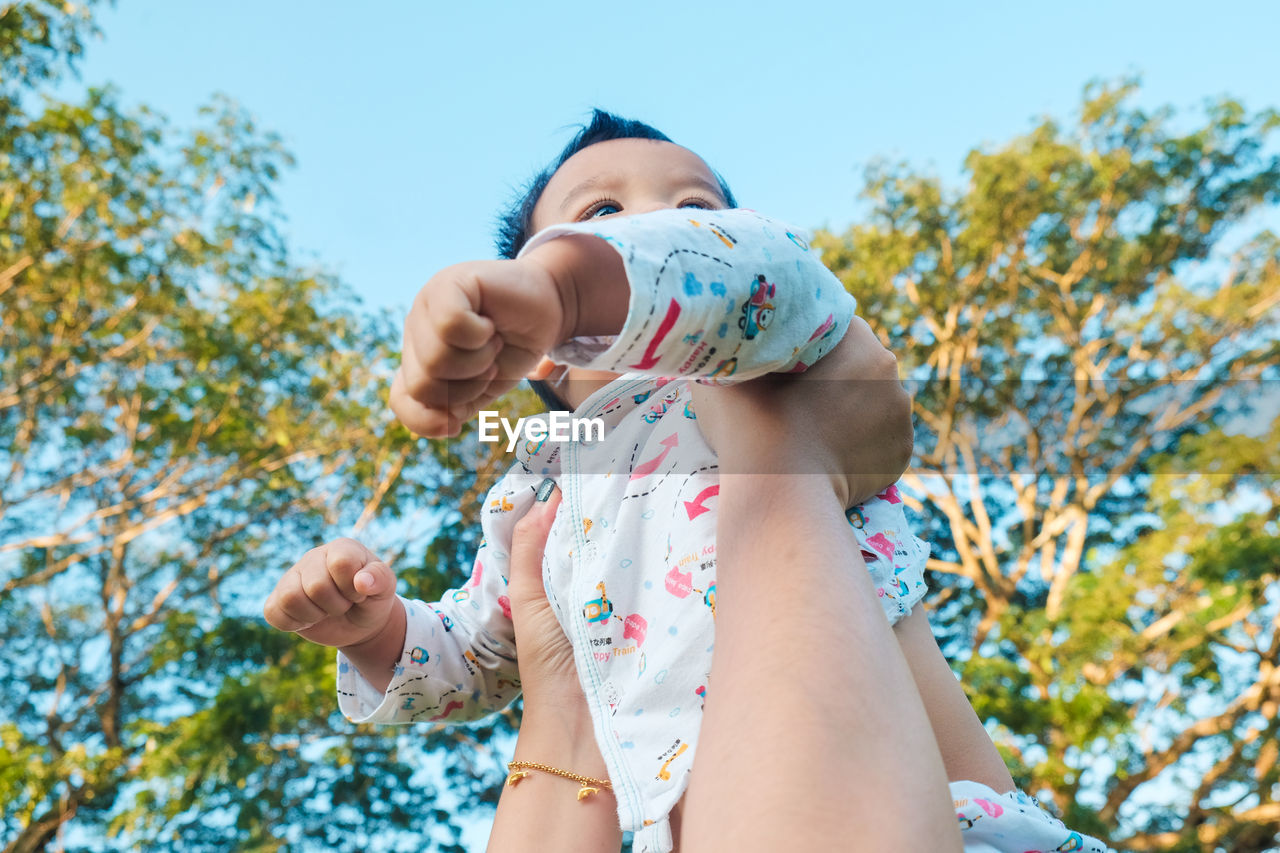 Cropped hand holding cute baby boy outdoors