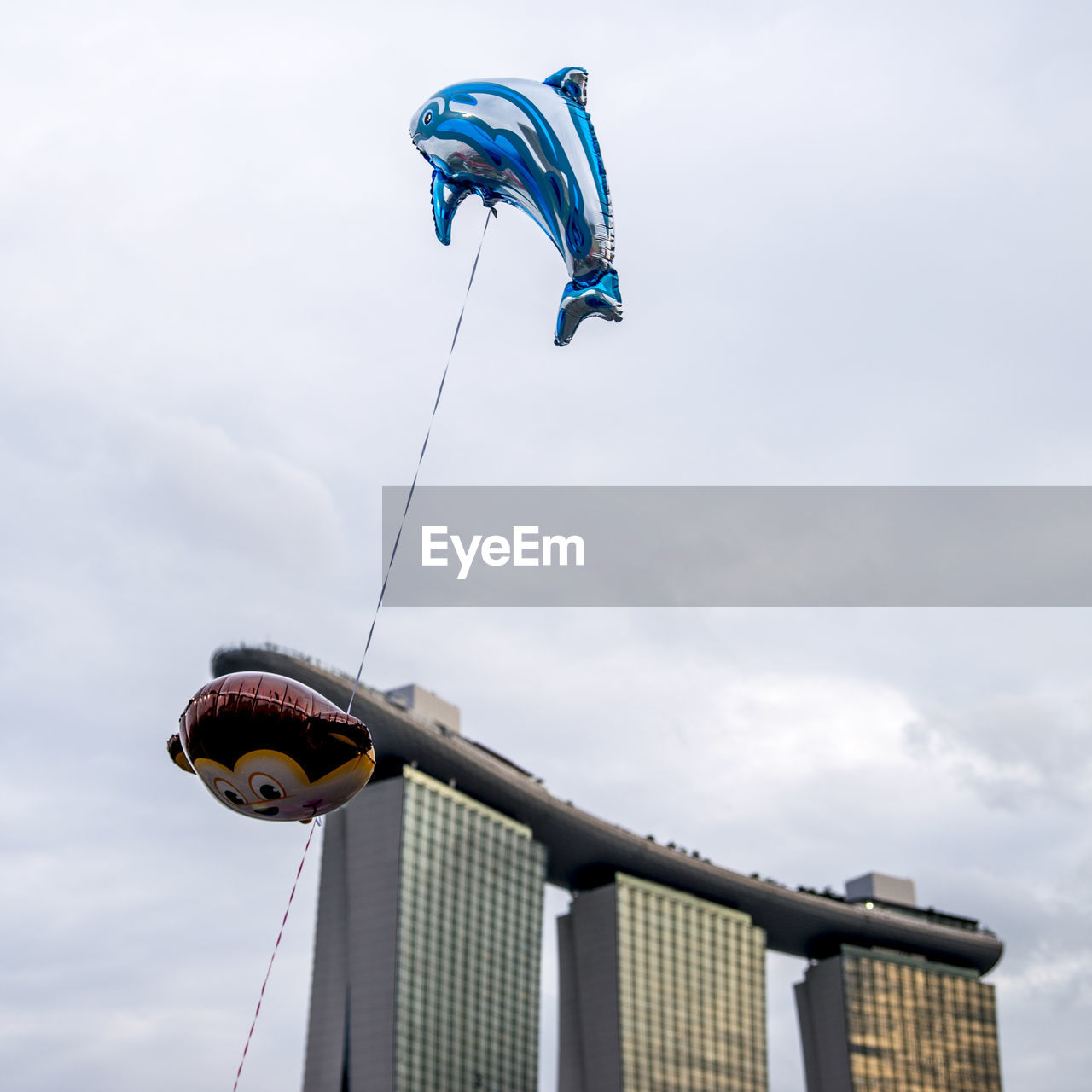 Low angle view of helium balloons flying against marina bay sands