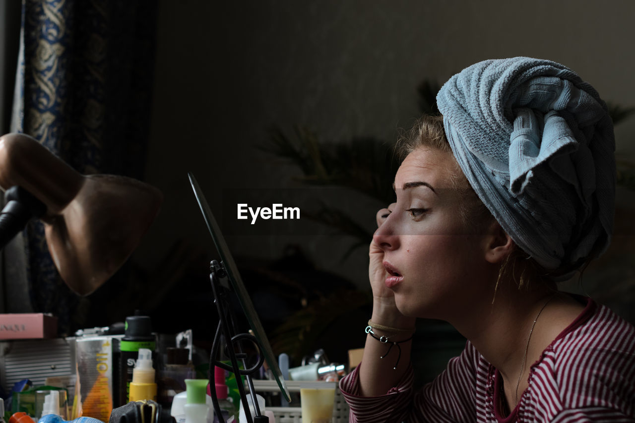 Profile view of young woman applying mascara at home