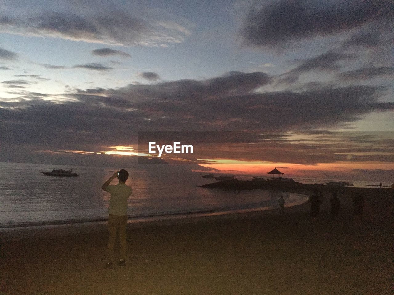 SILHOUETTE WOMAN PHOTOGRAPHING SEA AGAINST SKY AT SUNSET