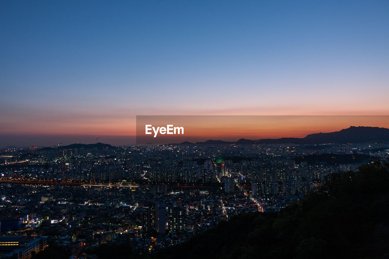 Mountain view of illuminated city against sky at sunset