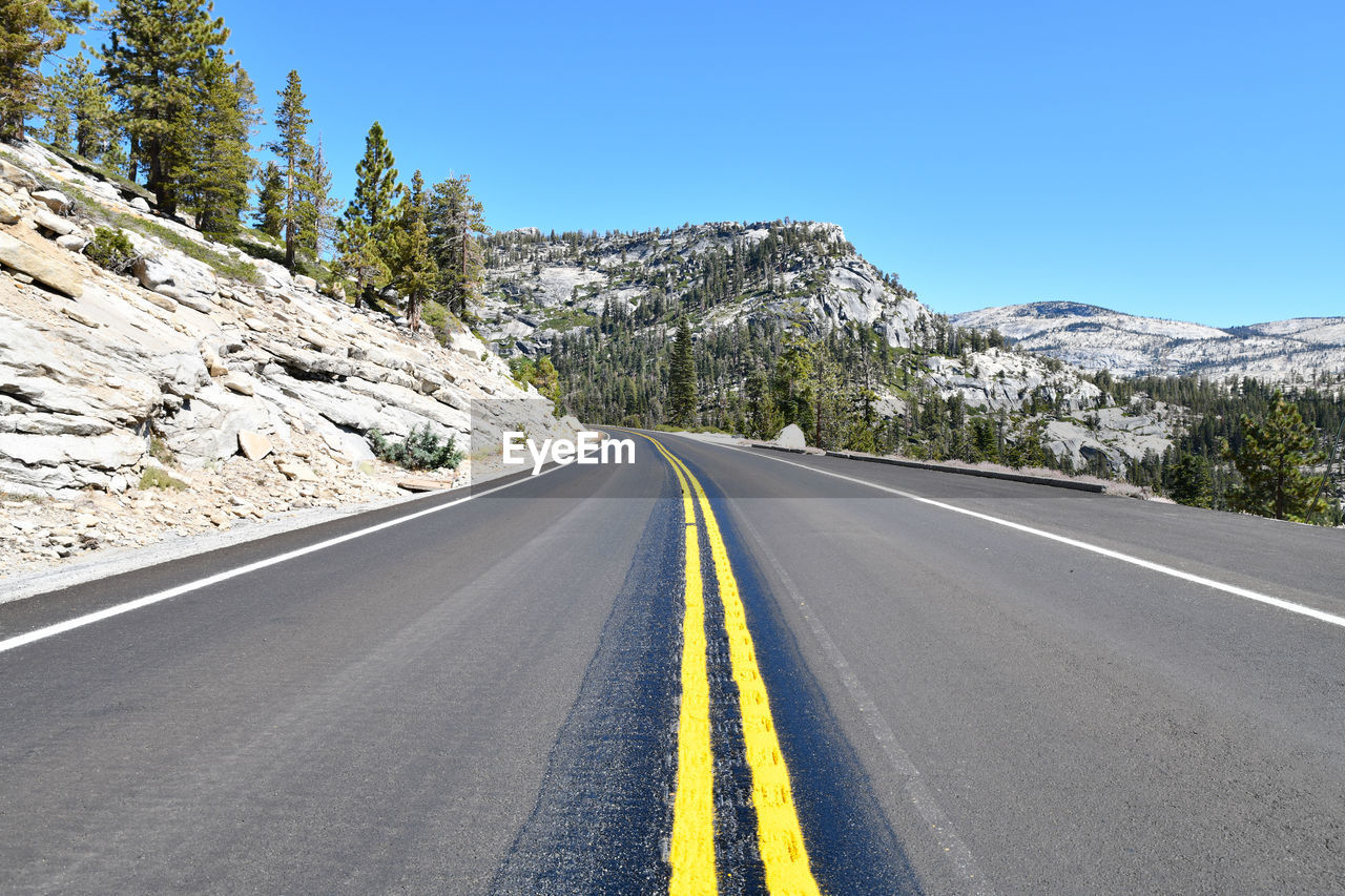 Road amidst trees and mountains against clear sky