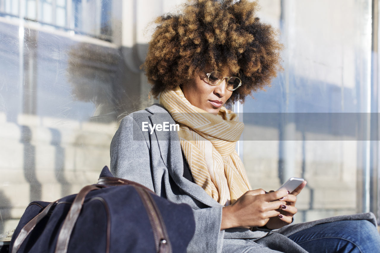 Woman using mobile phone while sitting at bus stop