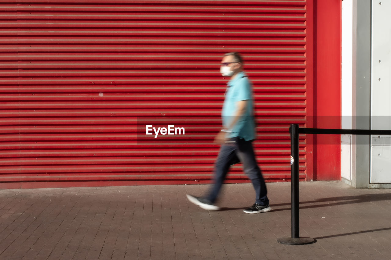 FULL LENGTH SIDE VIEW OF MAN WALKING ON RED WALL