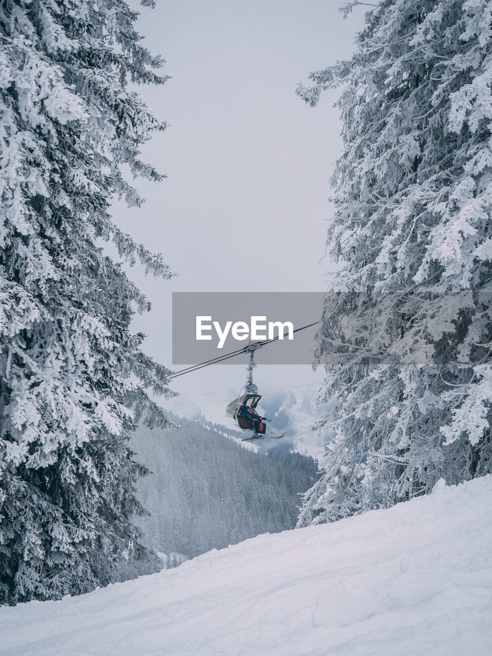 Low angle view of people on ski lift over snowcapped mountain against sky