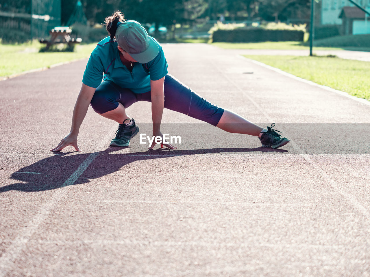 Athletic middle age woman stretching on red running track before training, healthy fitness lifestyle