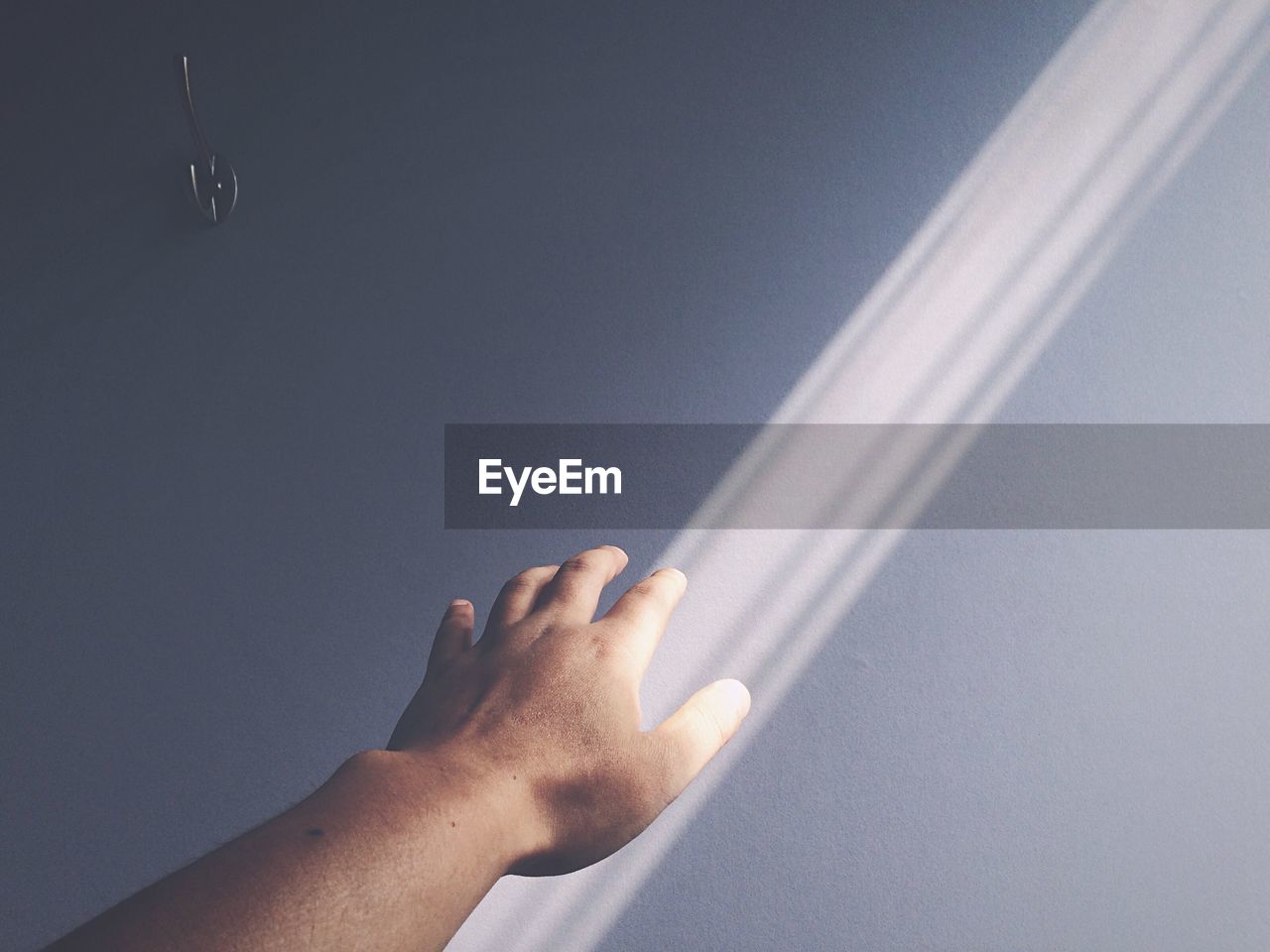 Cropped image of person touching sunlight falling on wall
