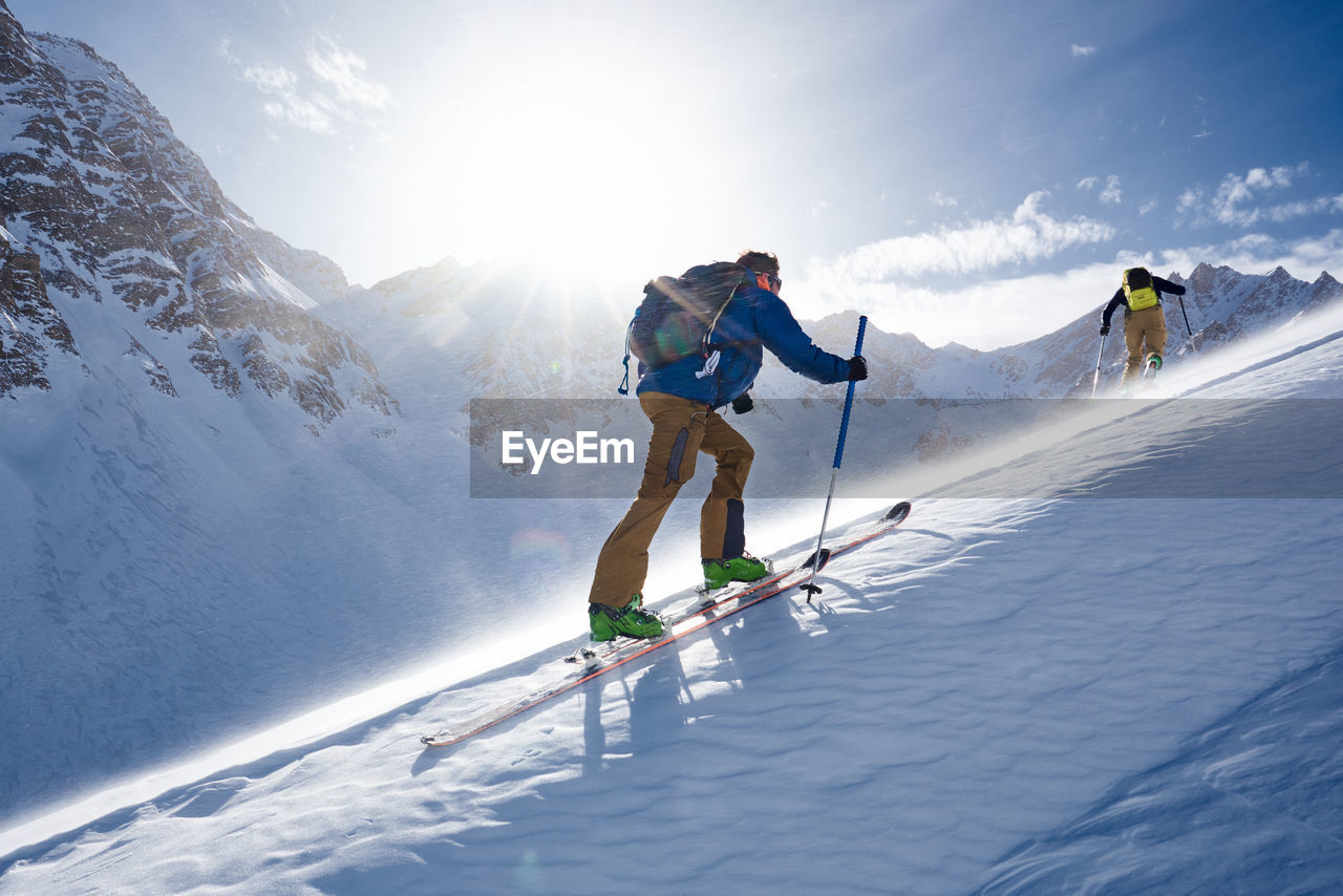 Man ski touring up hill in the wind and backlit by the sun