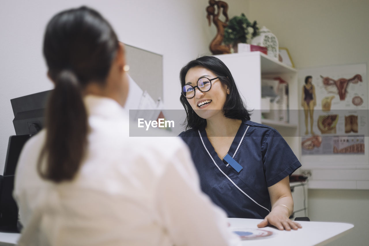 Happy female doctor wearing eyeglasses discussing with patient in medical clinic