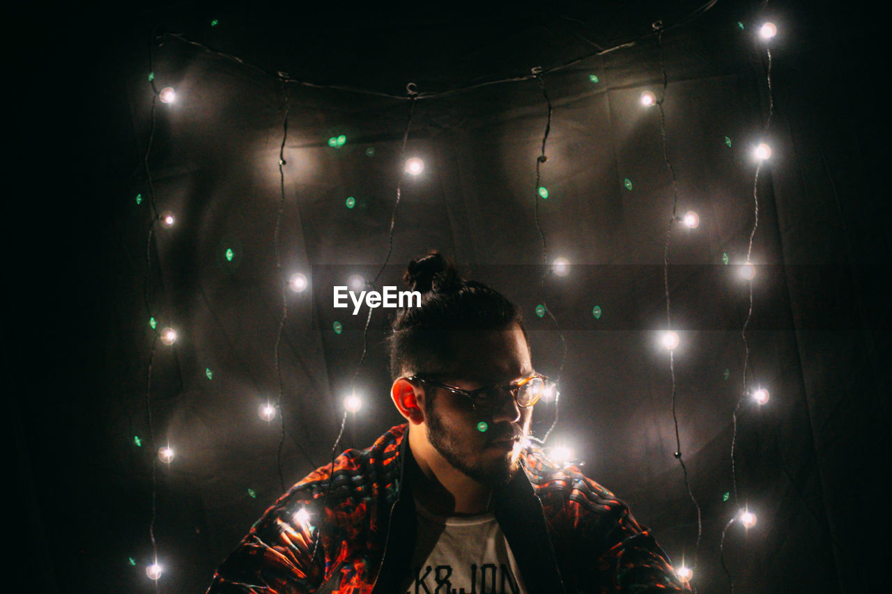 Man amidst illuminated fairy lights against wall