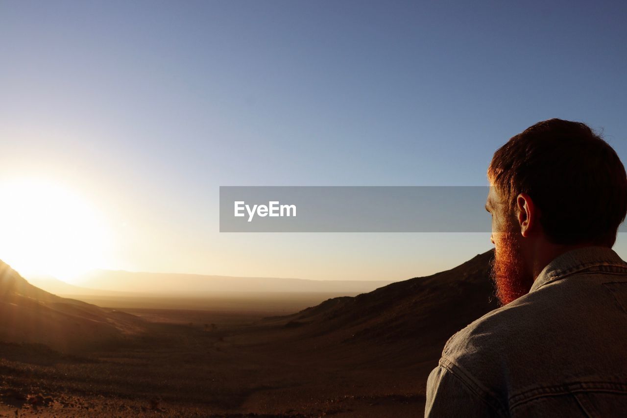 Rear view of man looking at mountains against sky