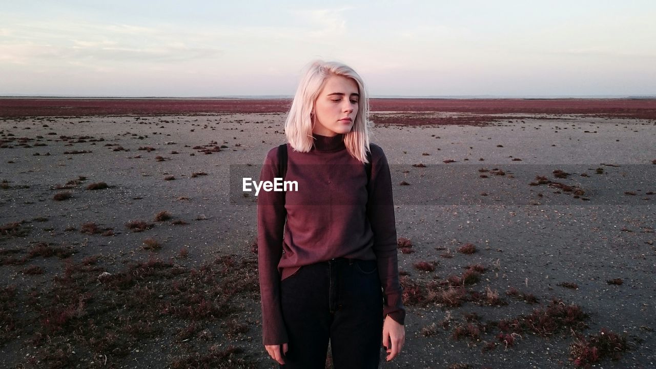 Thoughtful woman standing at beach against sky