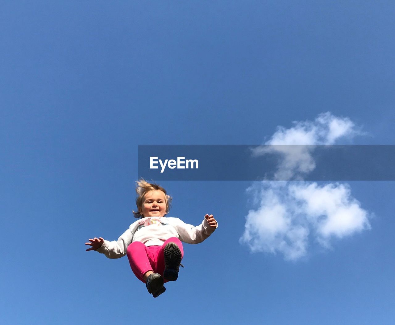 Low angle view of girl jumping against blue sky