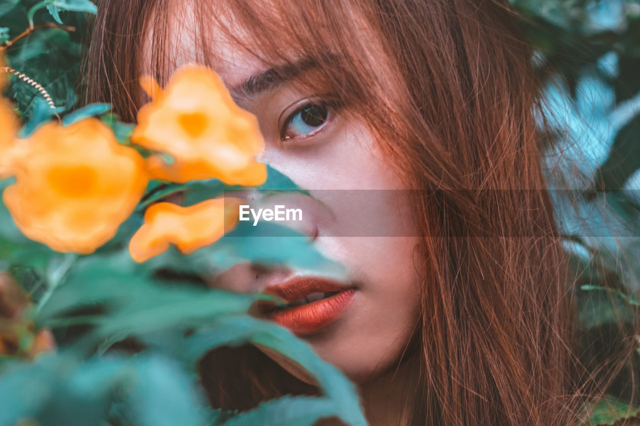 Close-up portrait of young woman with orange flowers