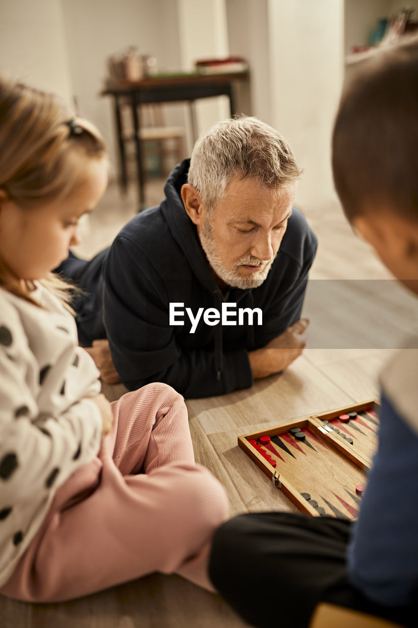 Grandfather lying on floor playing backgammon with grandchildren at home