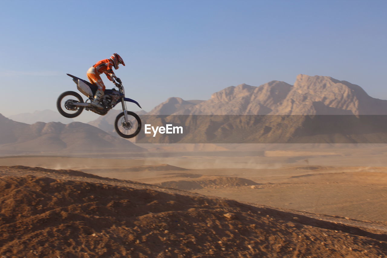 natural environment, transportation, sports, one person, extreme sports, mode of transportation, motion, adventure, stunt, full length, motorcycle, nature, sky, mid-air, headwear, helmet, motocross, mountain, sports helmet, environment, skill, leisure activity, land, landscape, activity, soil, vehicle, desert, riding, adult, jumping, men, scenics - nature, risk, sports equipment, side view, clear sky, crash helmet, speed, copy space, mountain biking, outdoors, travel, day, cycle sport, joy, exhilaration, off-road vehicle, sand, communication, warning sign