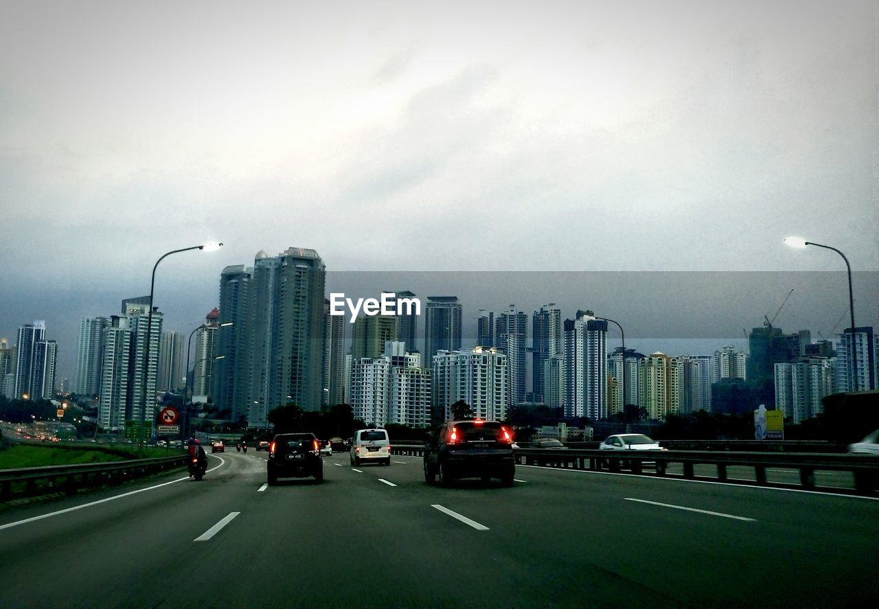 Cars on street against buildings and sky at dusk in city