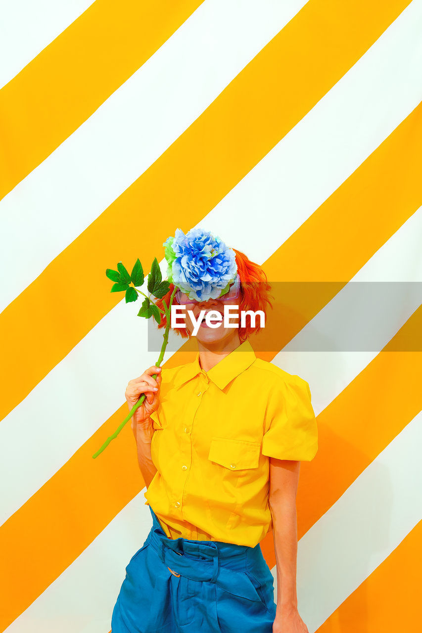 Smile woman on trend striped yellow background with flower in her hands. minimal 