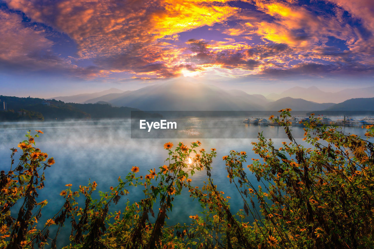 SCENIC VIEW OF LAKE BY MOUNTAINS AGAINST SKY AT SUNSET