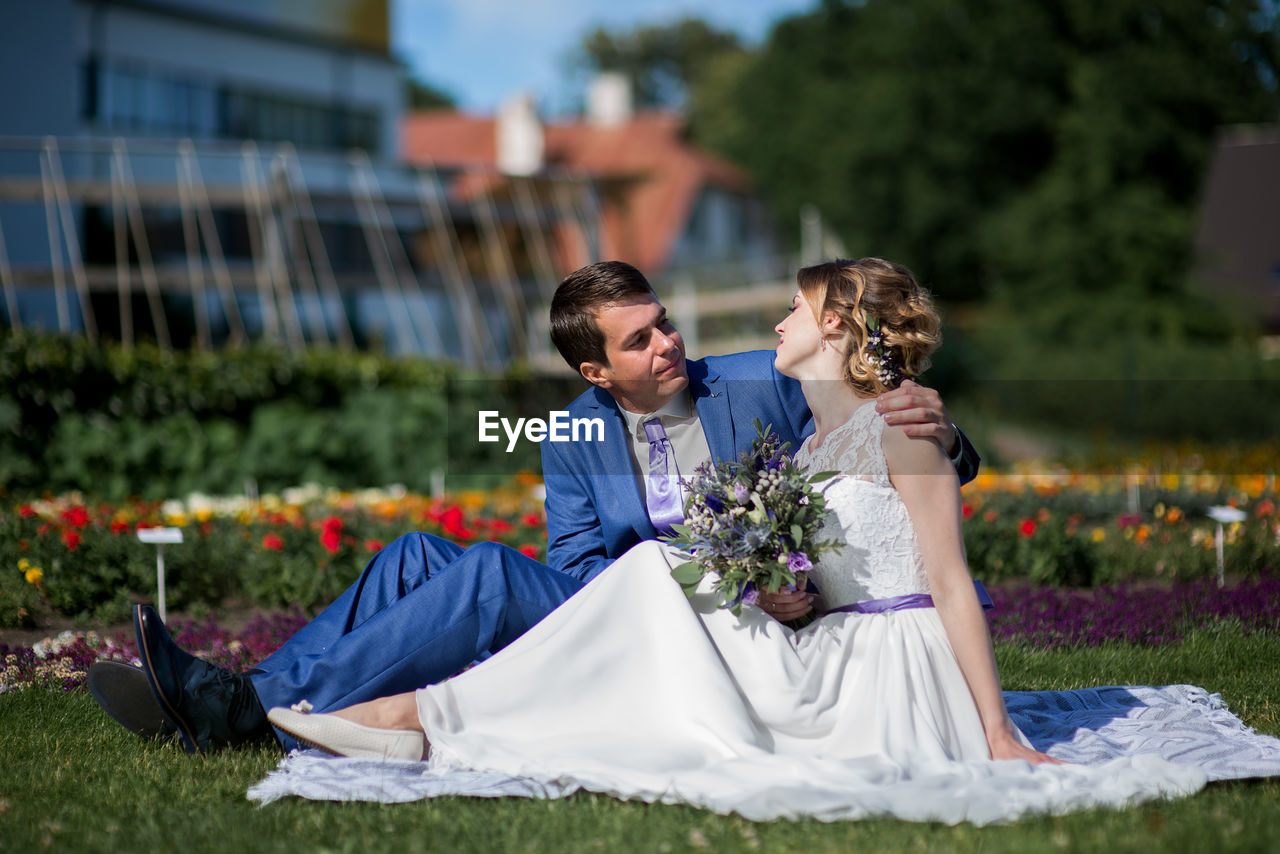 Bride and bridegroom sitting on picnic blanket at park