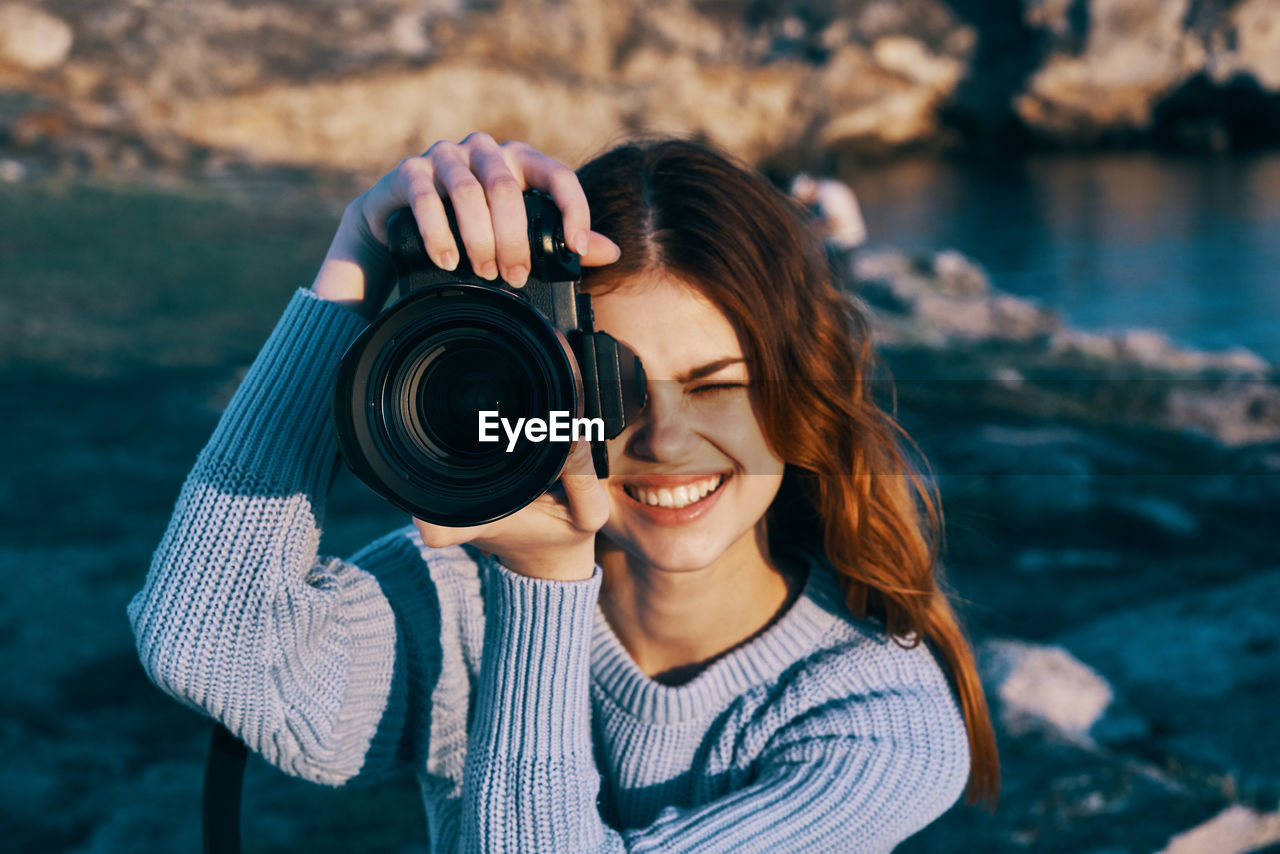 PORTRAIT OF SMILING YOUNG WOMAN PHOTOGRAPHING CAMERA