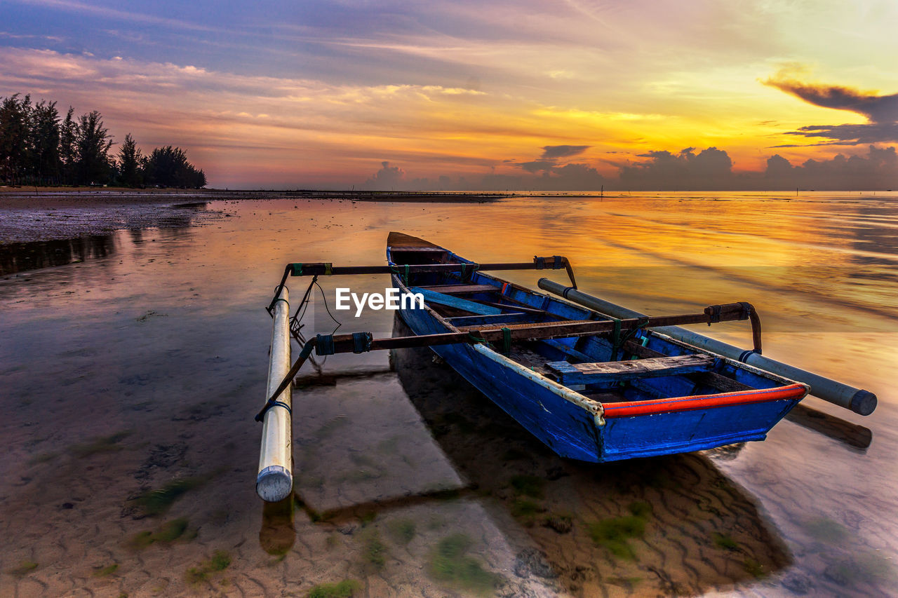 Boat moored at lake against sky during sunrise