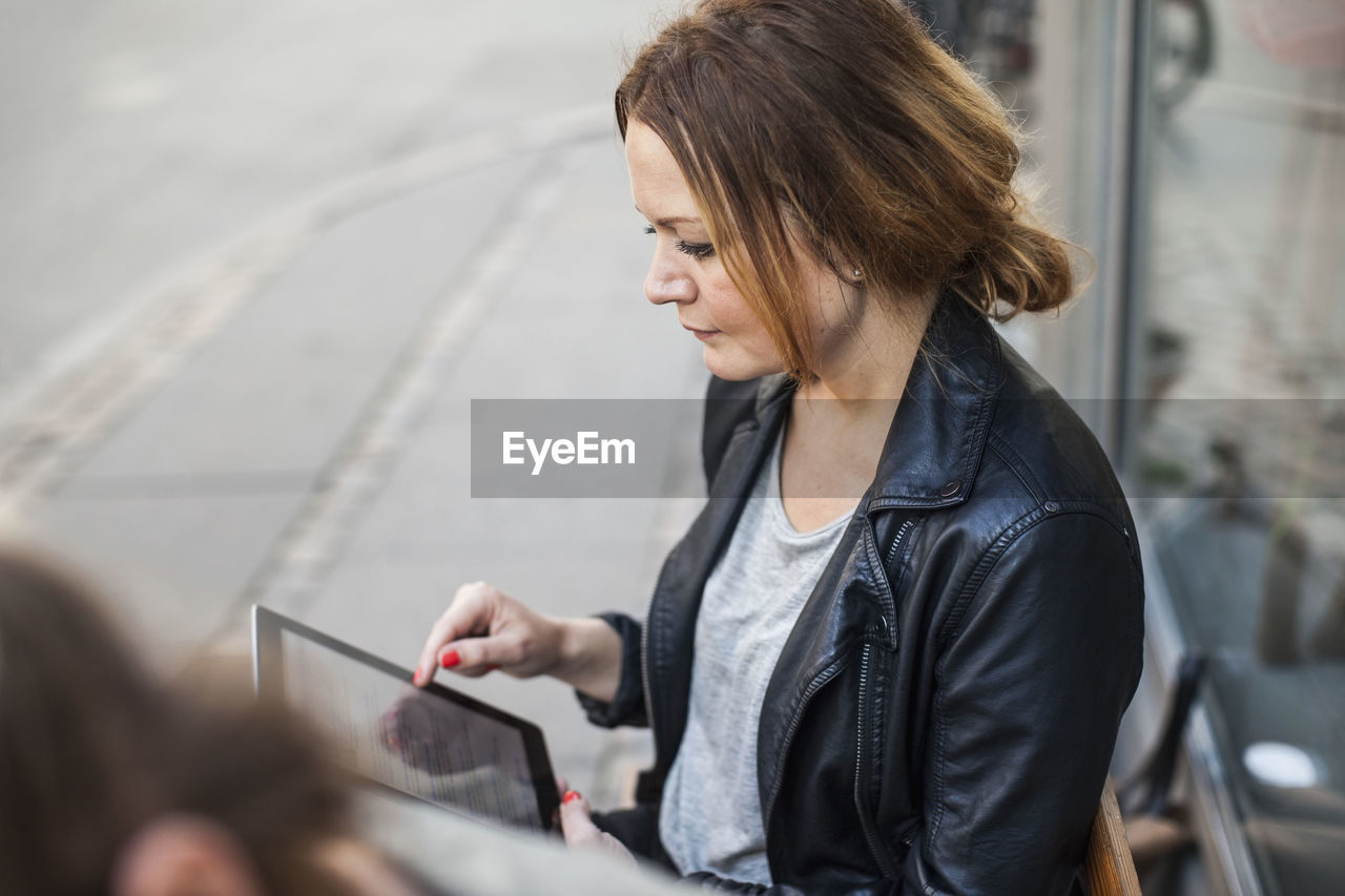 Mid adult woman using digital tablet on sidewalk bench