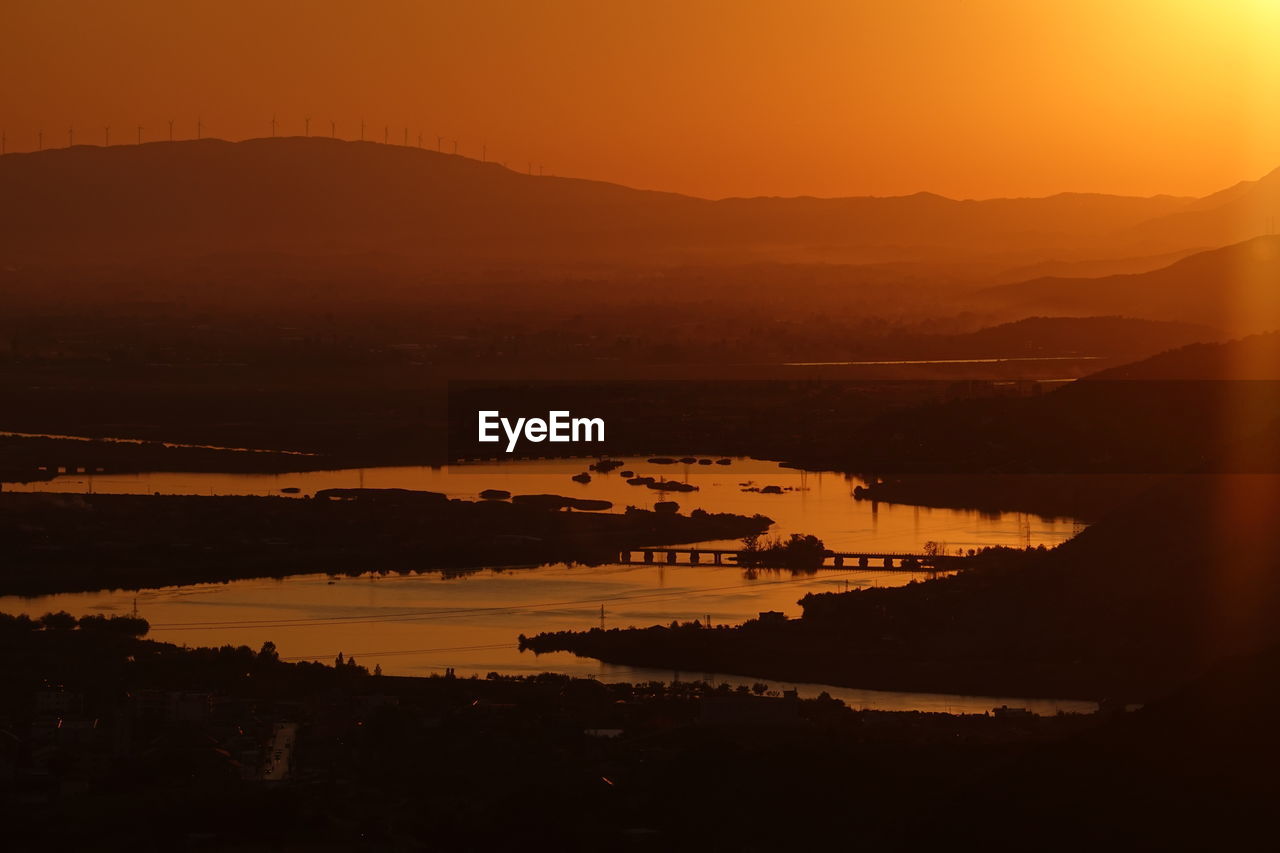 High angle view of silhouette city by sea against orange sky