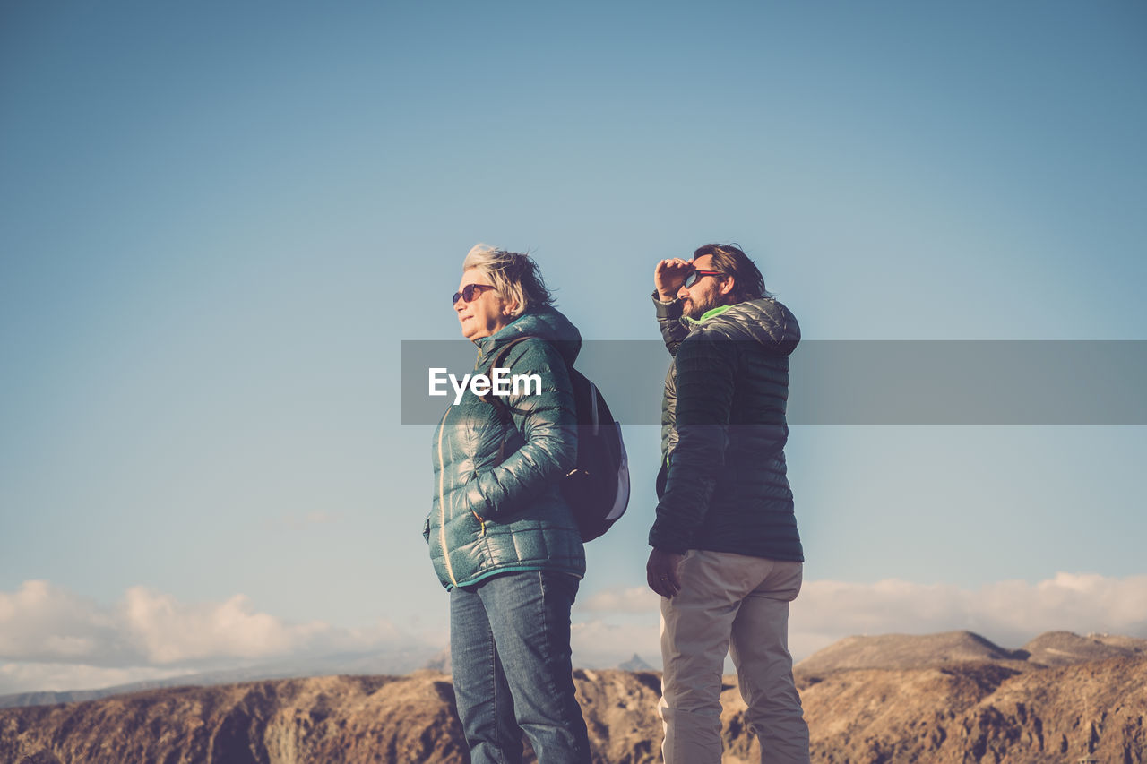 People looking away while standing against blue sky