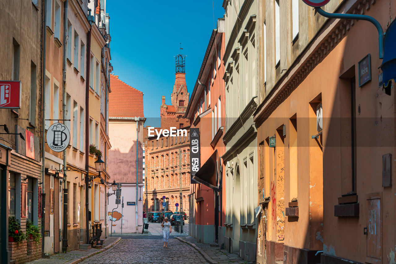 PEOPLE WALKING ON STREET AMIDST BUILDINGS AGAINST SKY