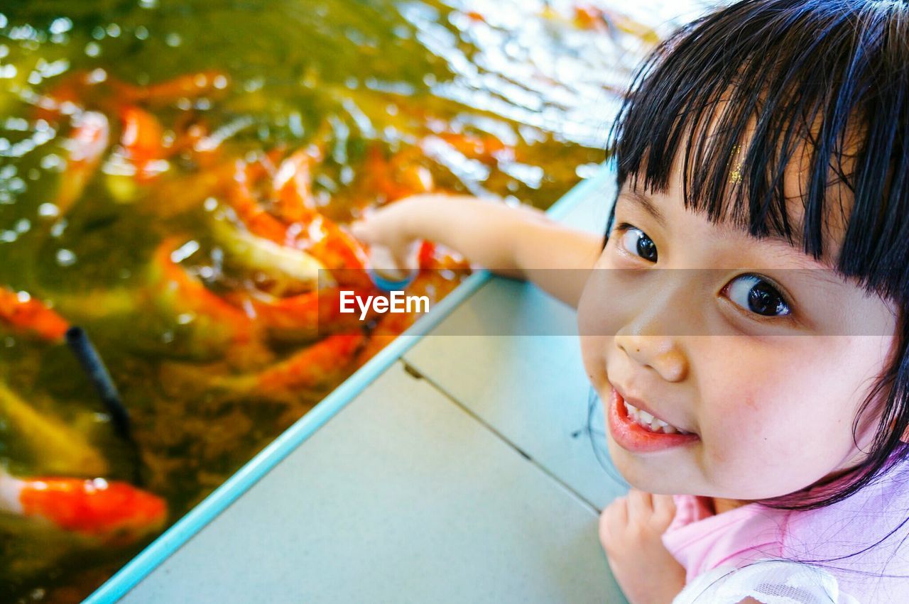 Close-up portrait of cute girl feeding koi carps in pond