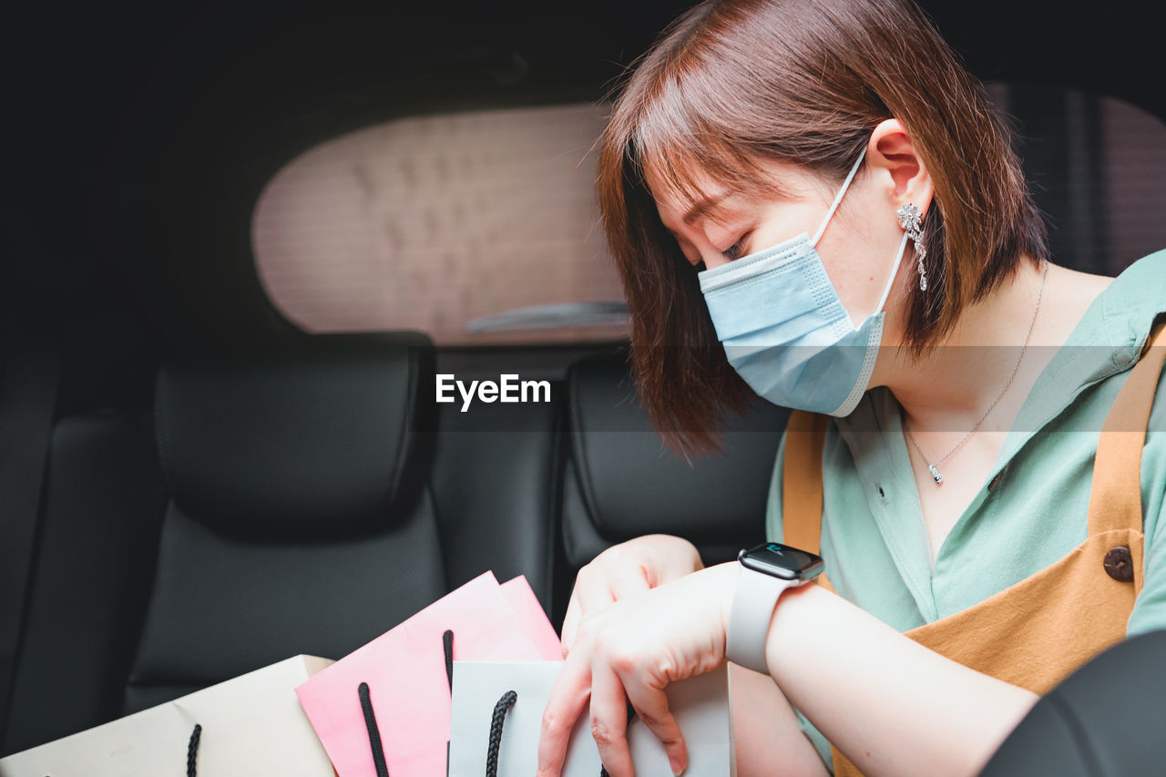 Close-up of woman wearing mask sitting with shopping bags in car