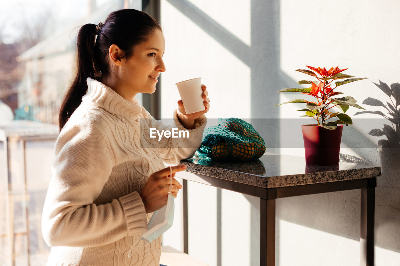 YOUNG WOMAN DRINKING COFFEE ON WINDOW AT HOME