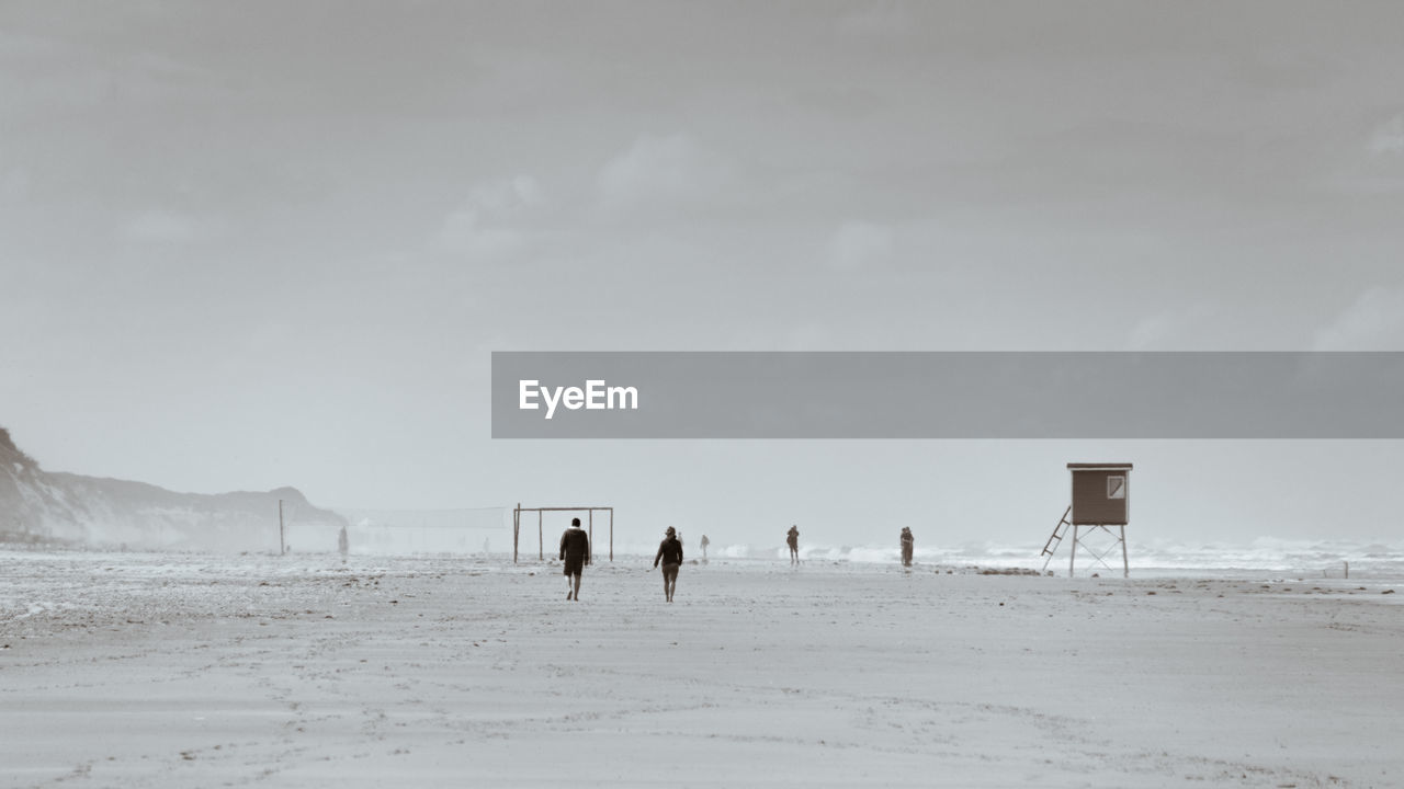 PEOPLE STANDING AT BEACH AGAINST SKY