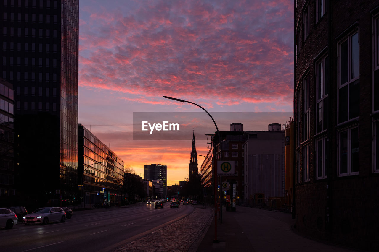 STREET AMIDST BUILDINGS AGAINST SKY AT SUNSET