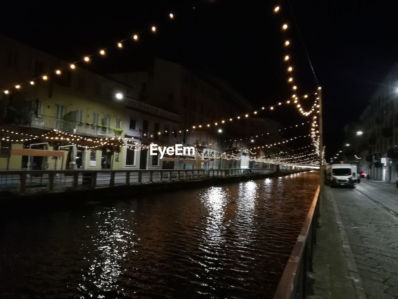 ILLUMINATED STREET BY RIVER AND BUILDINGS AT NIGHT