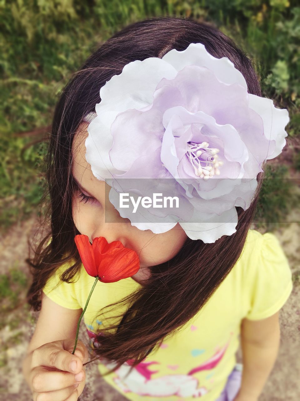 High angle view of little girl wearing headband while smelling poppy flower