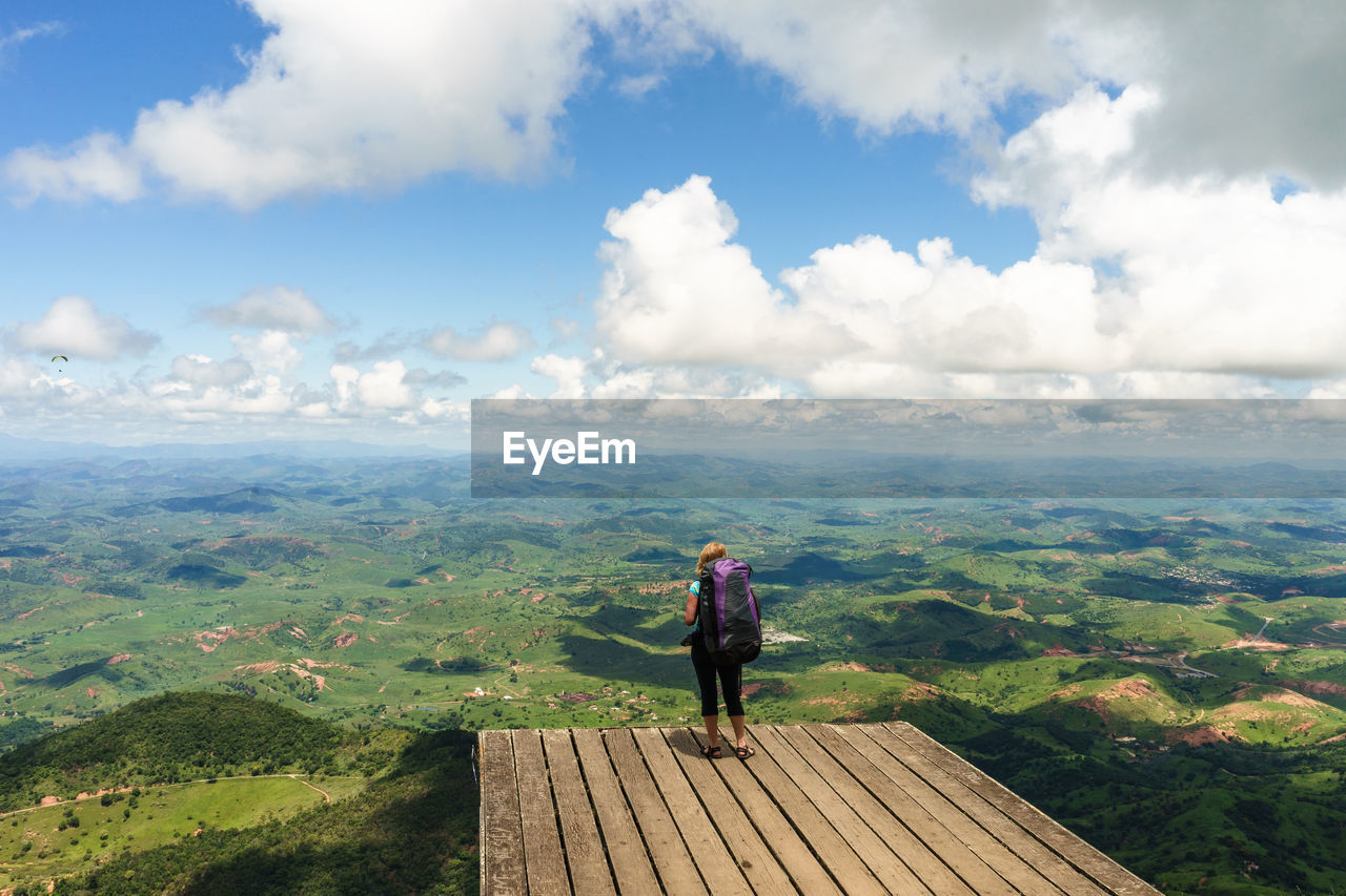 Woman standing on boardwalk against landscape in sunny day