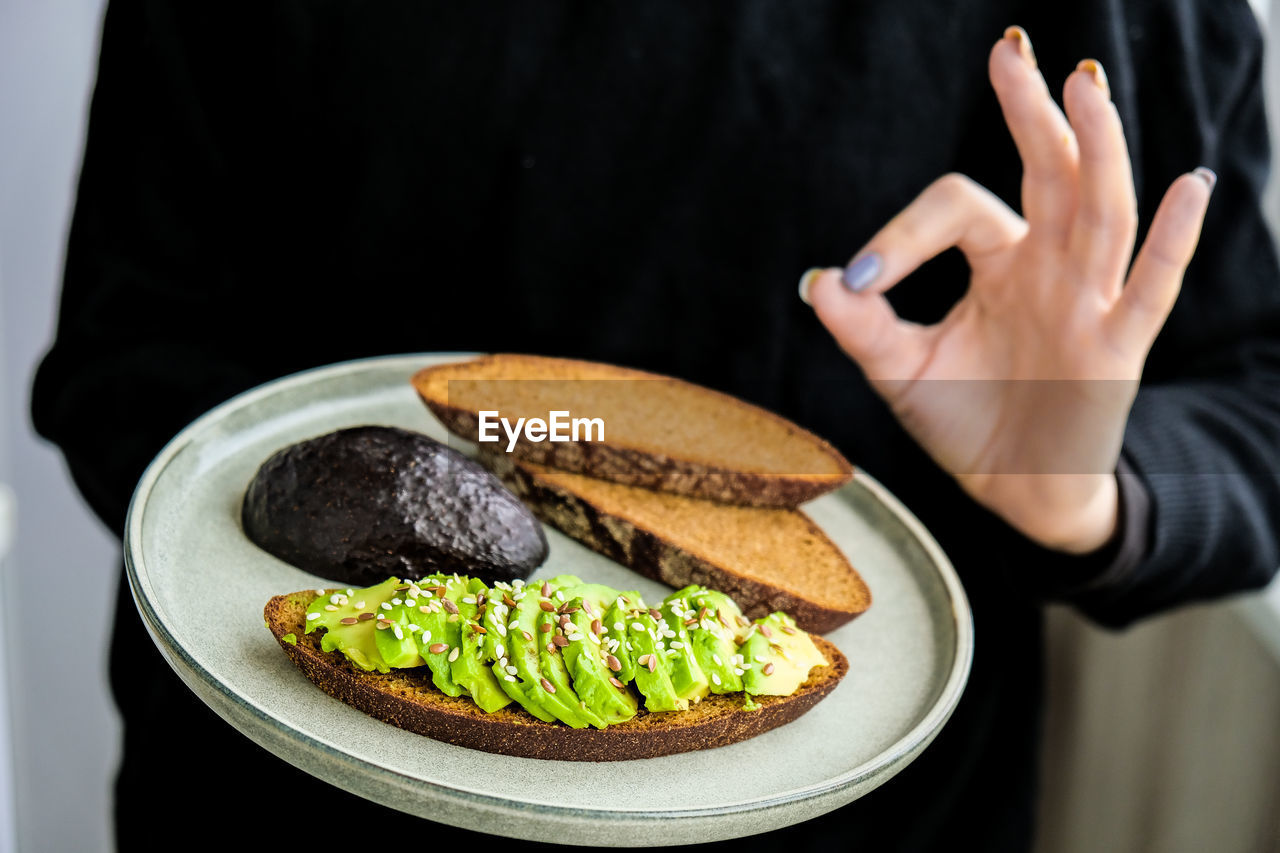 Female hand holding plate with ingredients for healthy avocado toast. ripe hass avocado, wholegrain