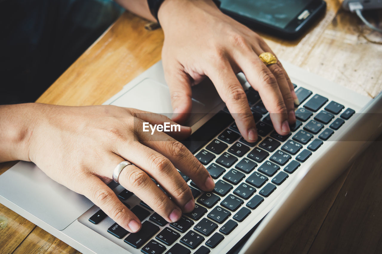 Cropped hands of man using laptop at table