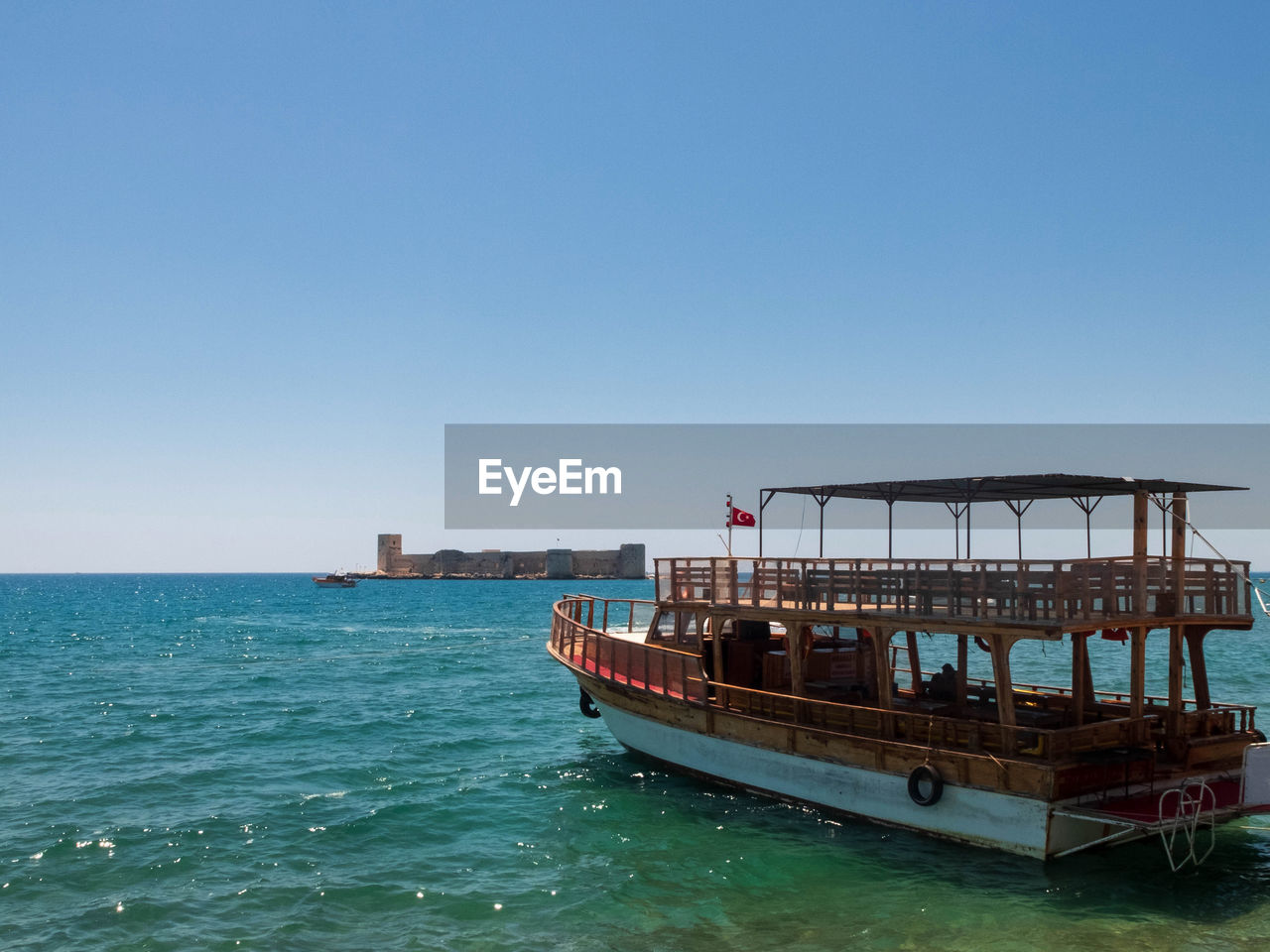 Ferryboat with turkish flag against maiden's castle or kizkalesi. kizkalesi, mersin province, turkey